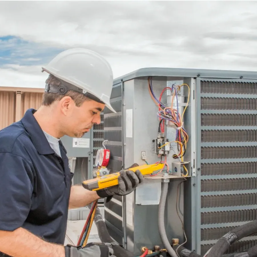 HVAC technician in a hard hat testing an outdoor air conditioner with a multimeter